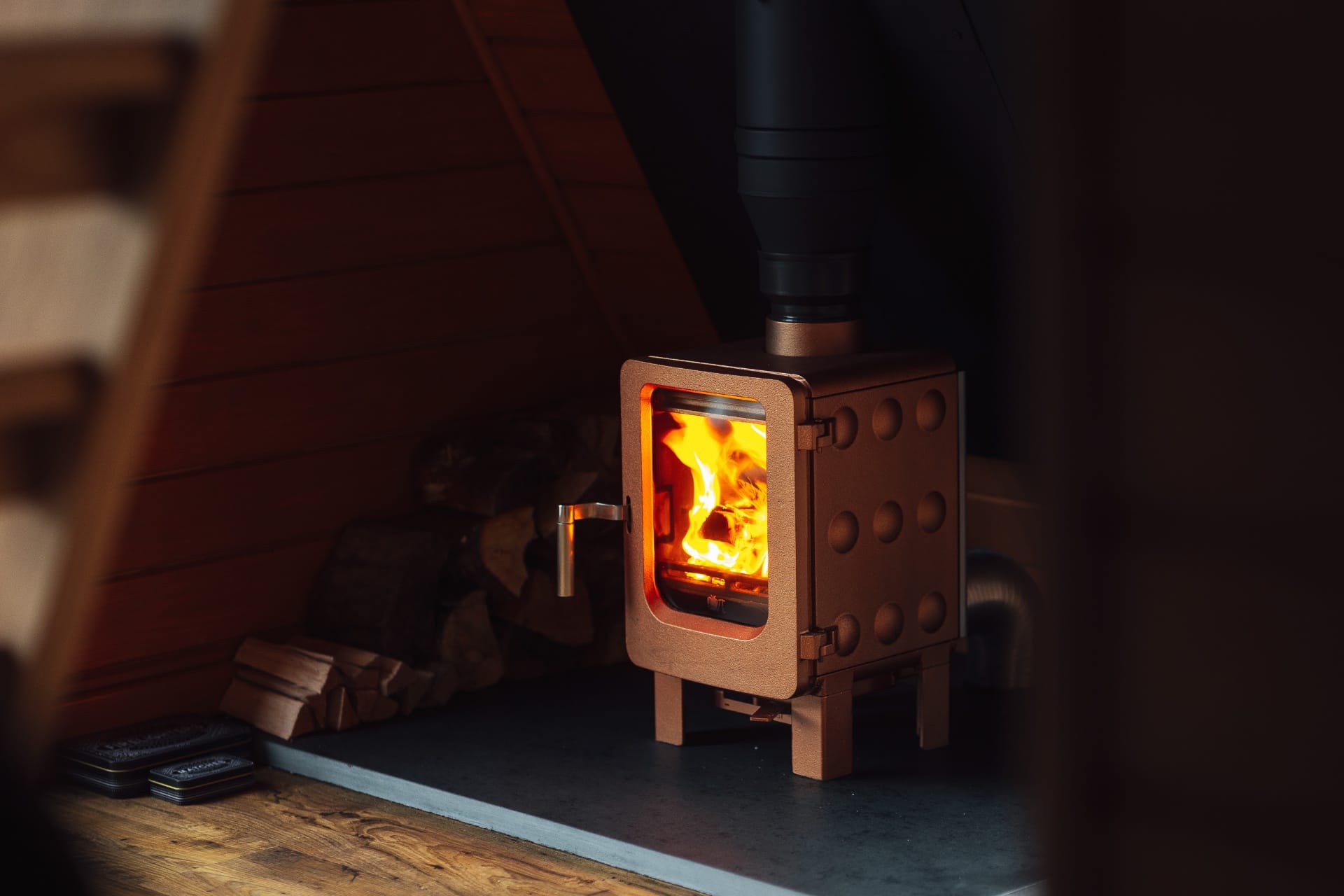 Wood burner glowing beside a stack of logs in the A-frame living space