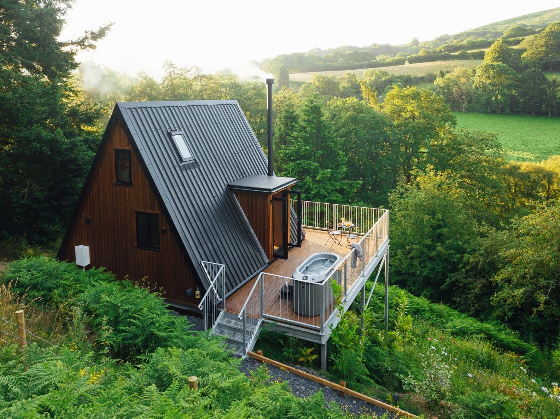 Aerial view of the A-frame cabin, deck and hot tub set among ferns and woodland