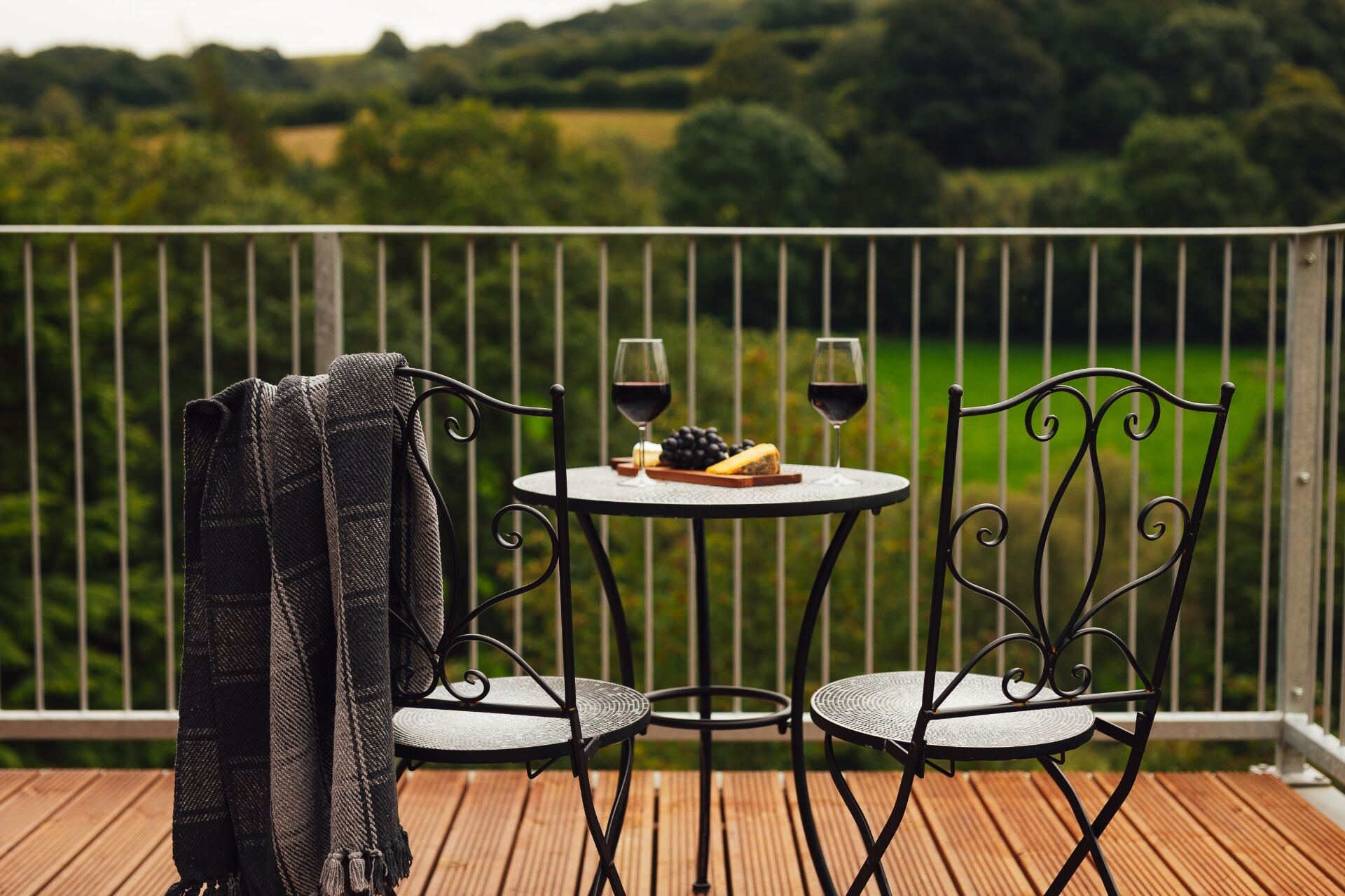 Bistro table on the deck set with red wine and a cheese board, looking out over green Welsh fields and woodland