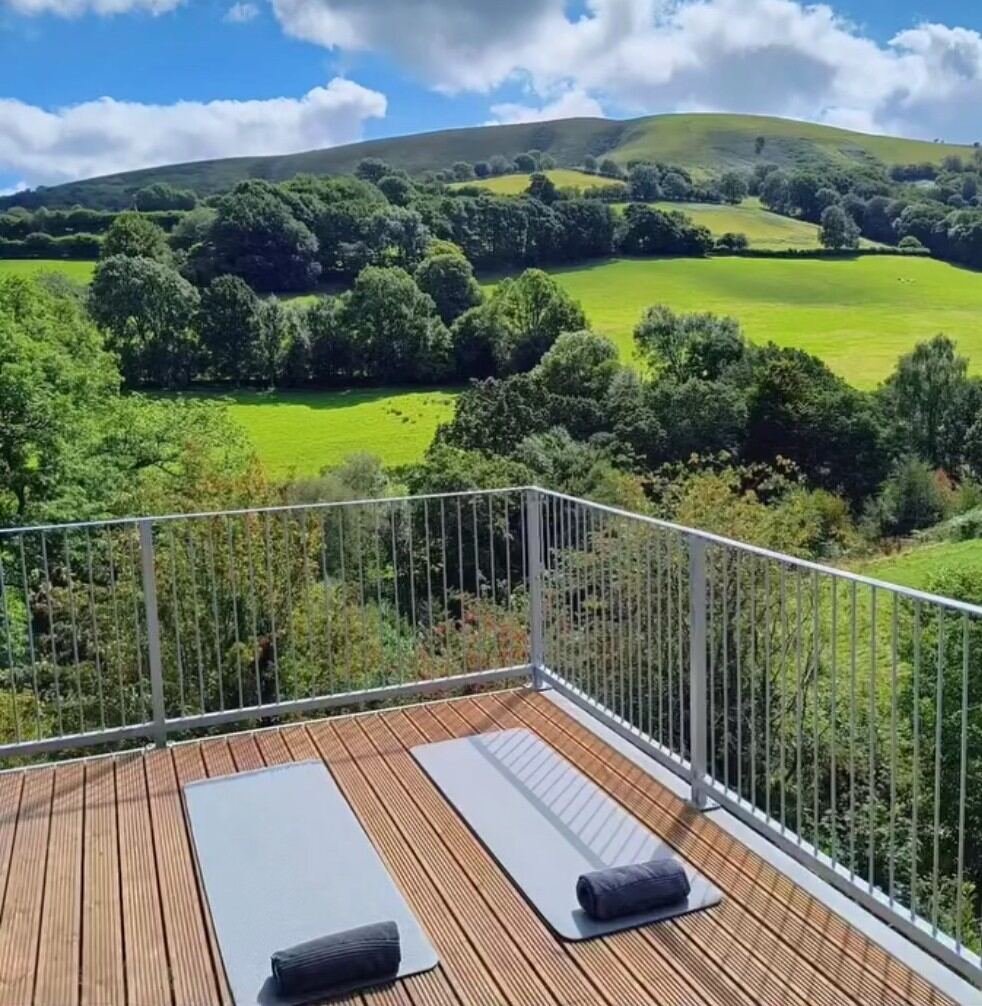 Two yoga mats laid out on the cabin deck looking across the green Welsh valley to the hills beyond