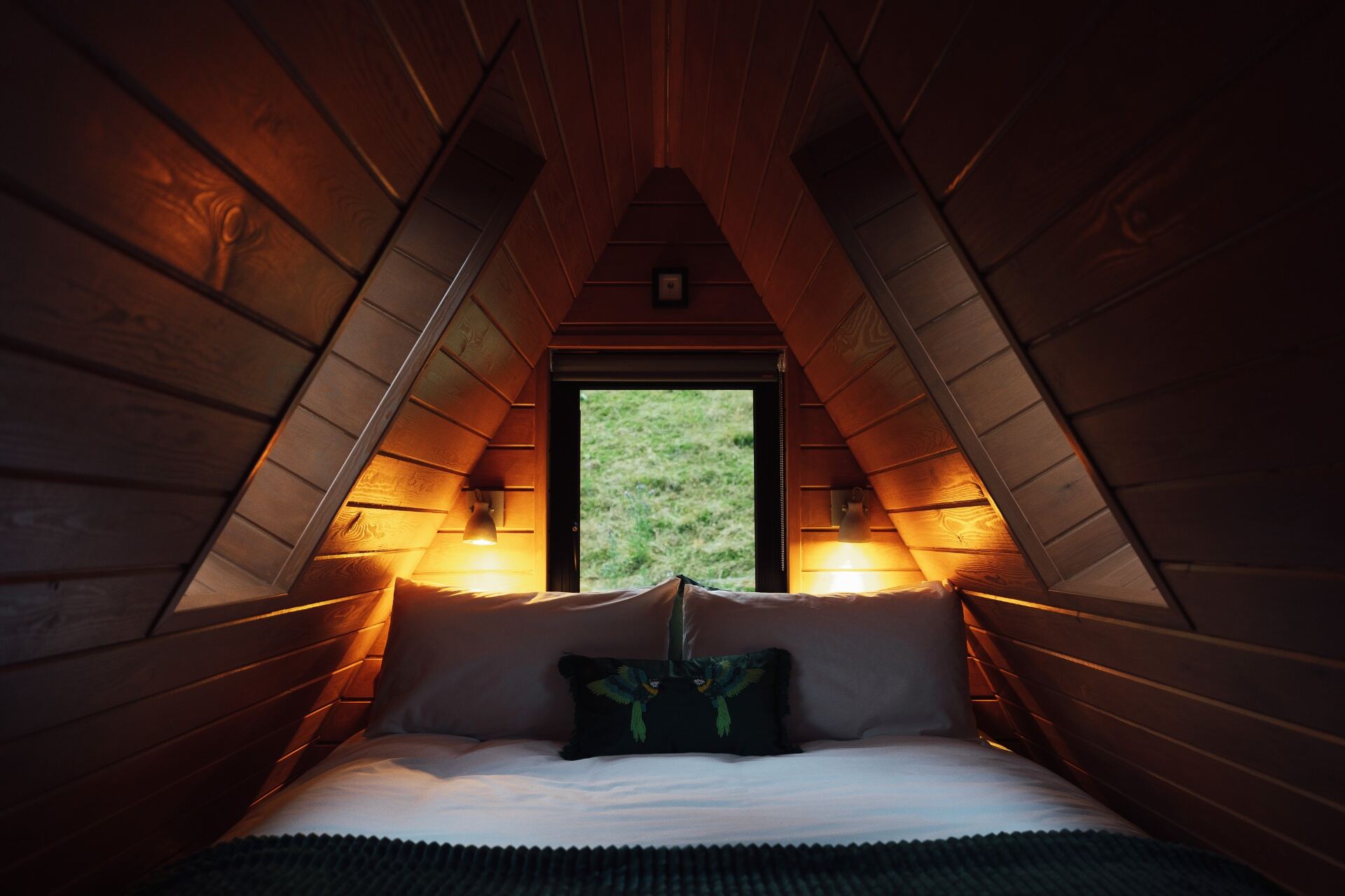 Cosy mezzanine bed under the A-frame rafters at The Perch with warm wall lights and valley view through the window